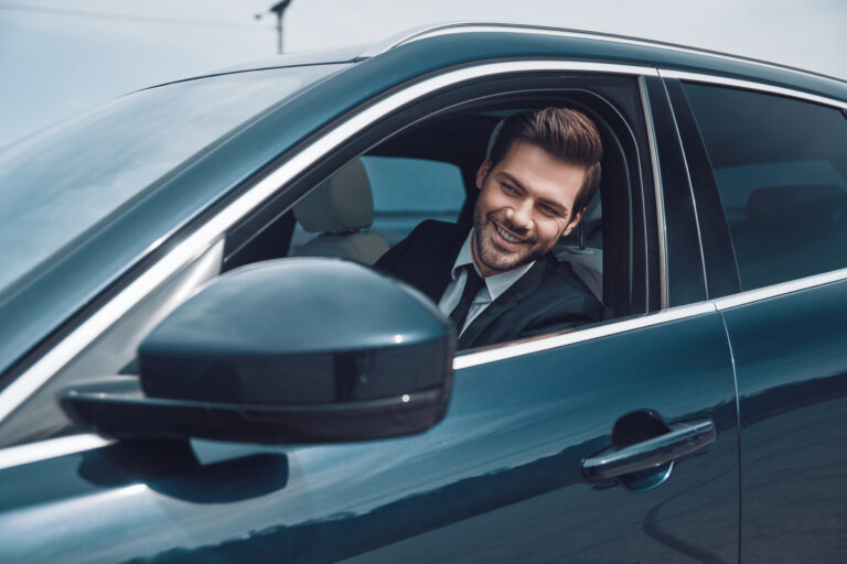 Happy driver. Handsome young man in full suit looking straight while driving a car