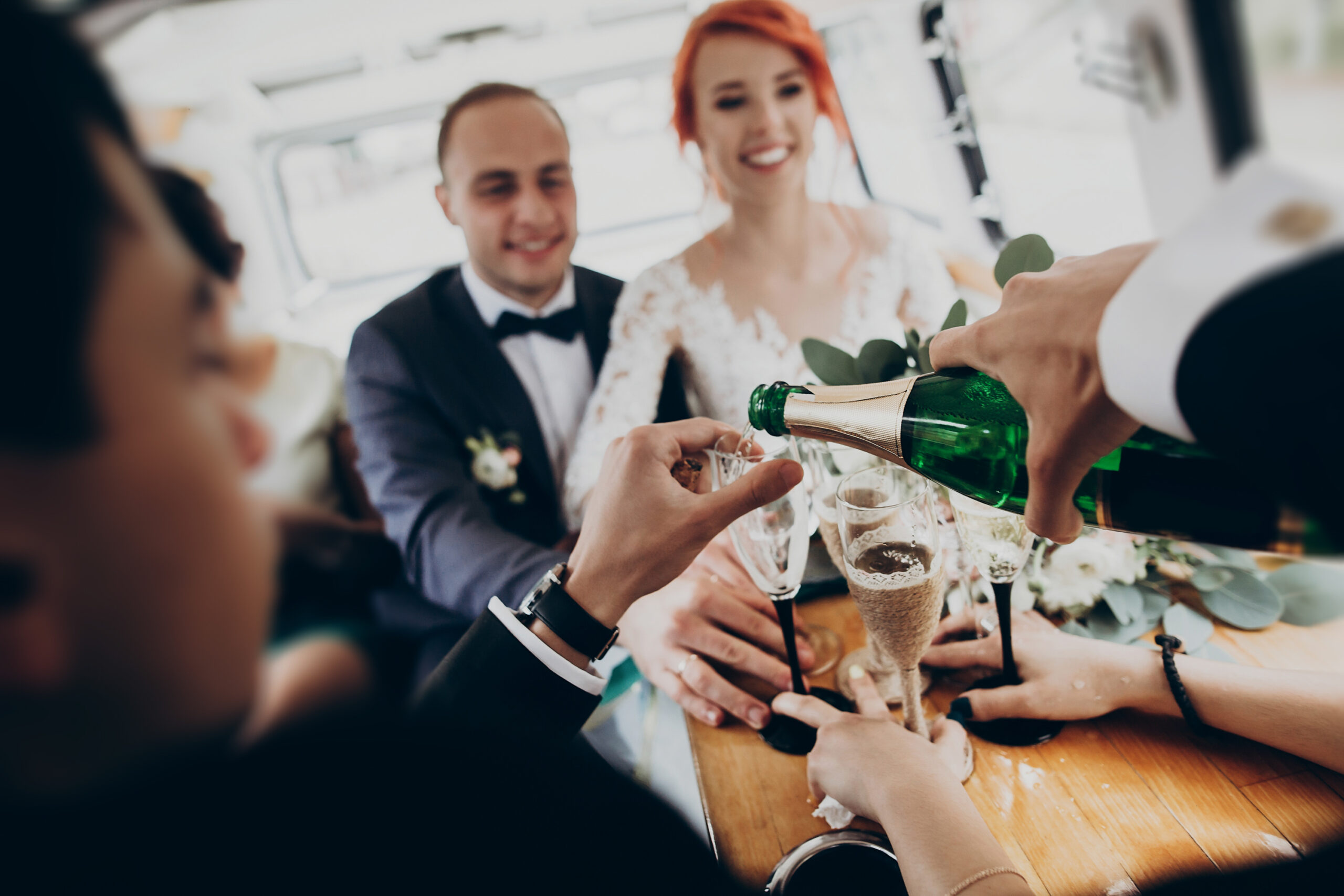 hands with glasses of champagne, stylish happy bride and groom toasting laughing and having fun with bridesmaids and groomsmen inside of retro car. emotional moment, space for text. wedding party